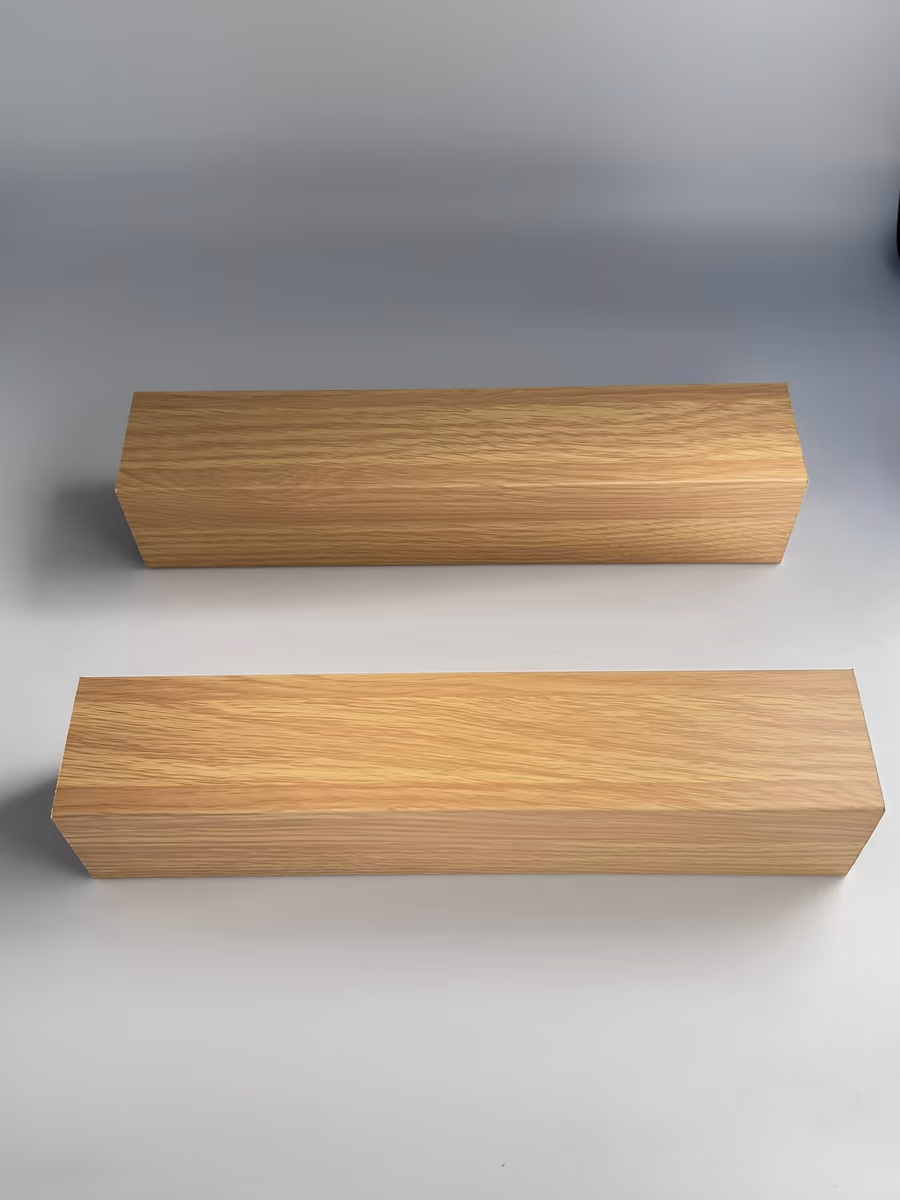 Two cut samples of a 2"x2" cold-rolled aluminum baffle in a light oak wood grain finish