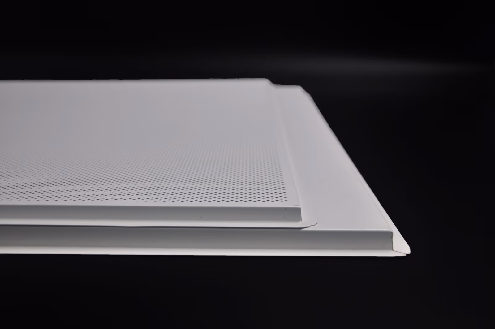 Two perforated aluminum lay-in panels stacked on a dark surface