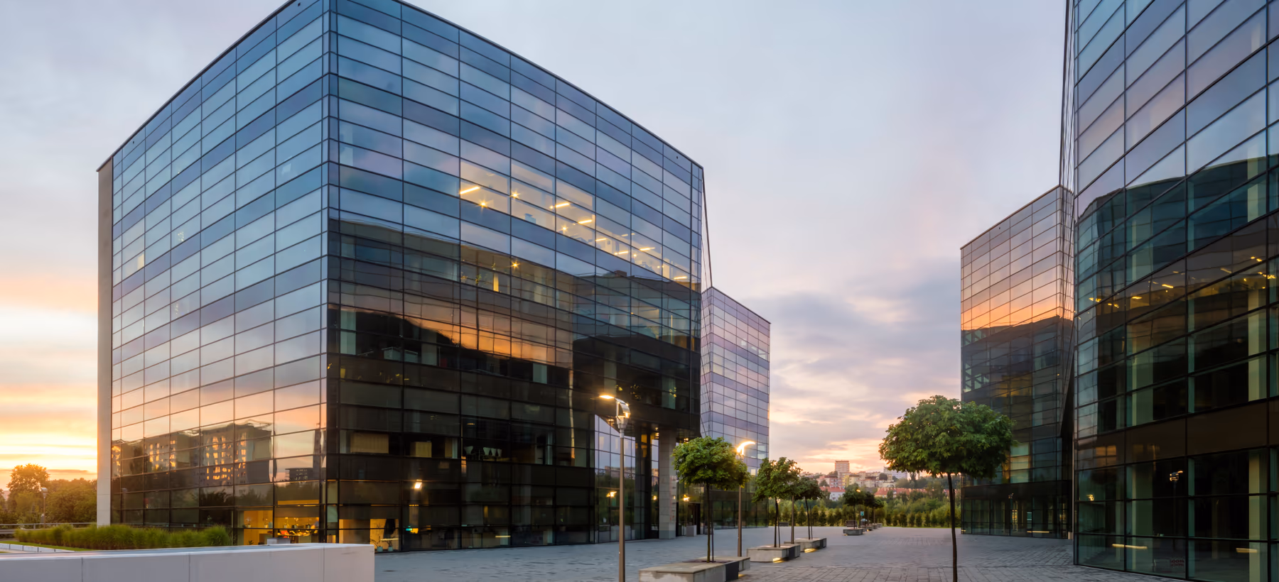 Glass-clad commercial office buildings around a paved plaza at dusk