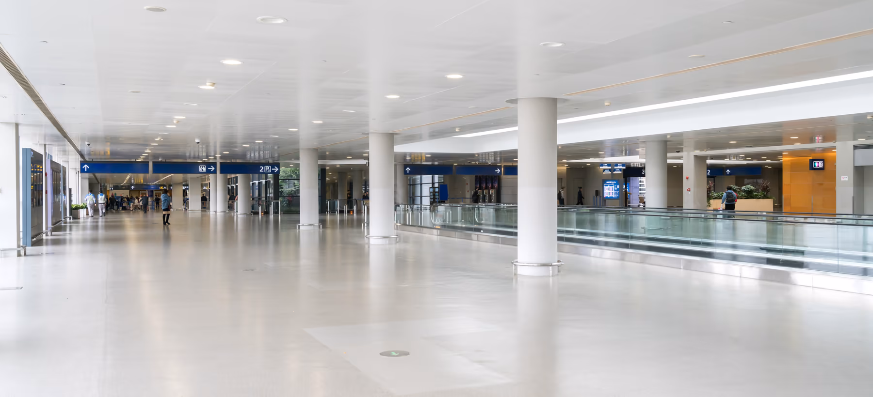 Airport concourse with a flat ceiling, gate signage and a moving walkway
